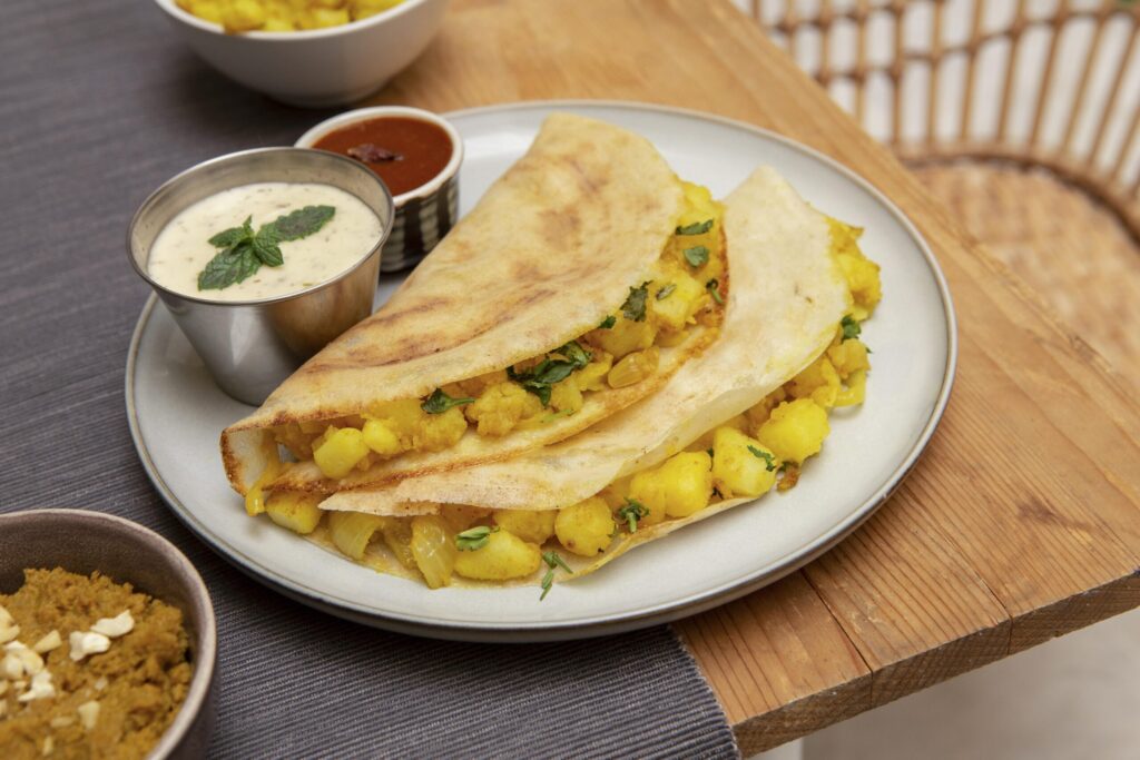 Crispy masala dosa filled with spiced potato stuffing, served with coconut chutney and tangy sambar on a plate